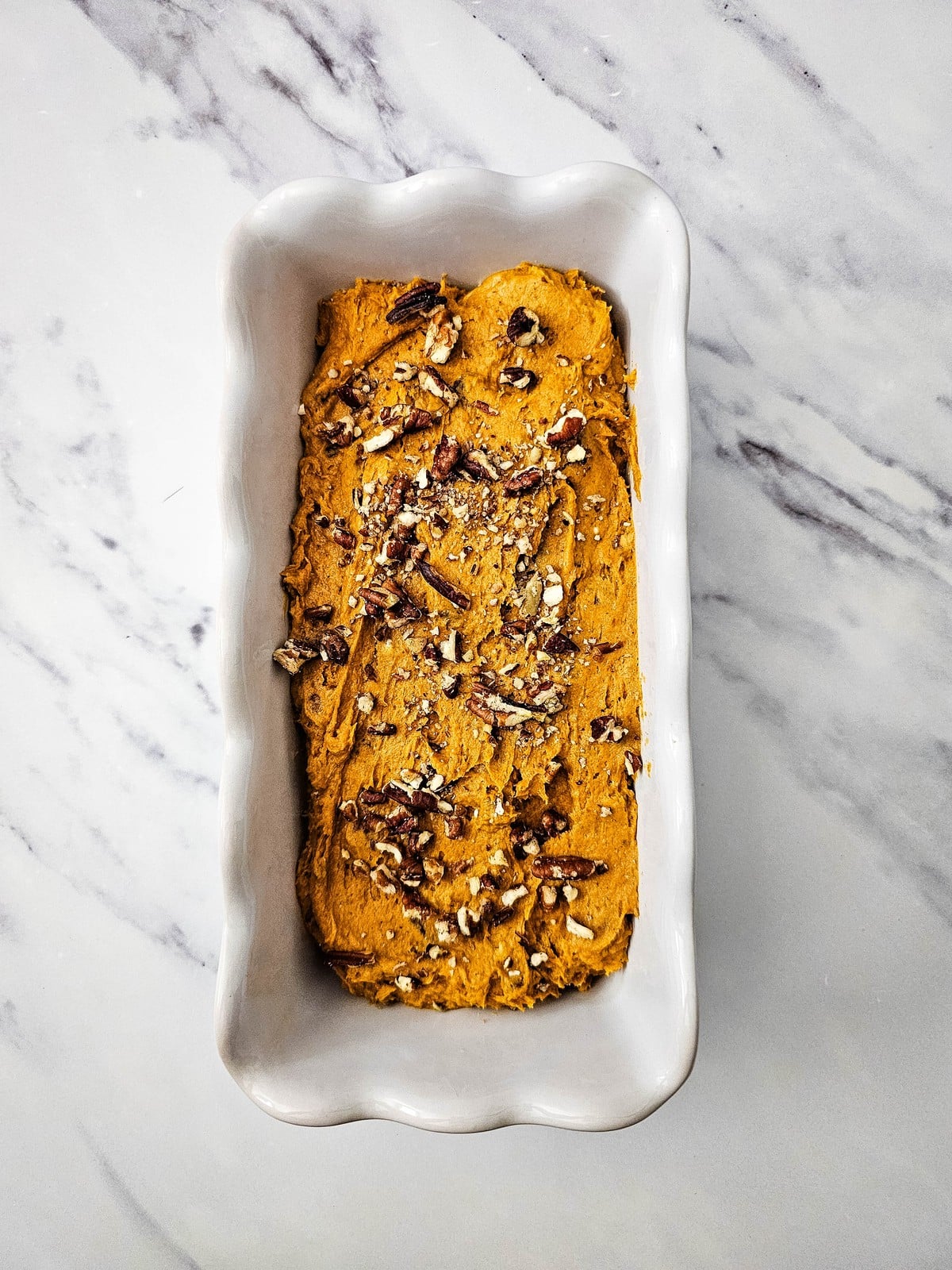 Reserved chopped pecans scattered over the top of the unbaked pumpkin bread