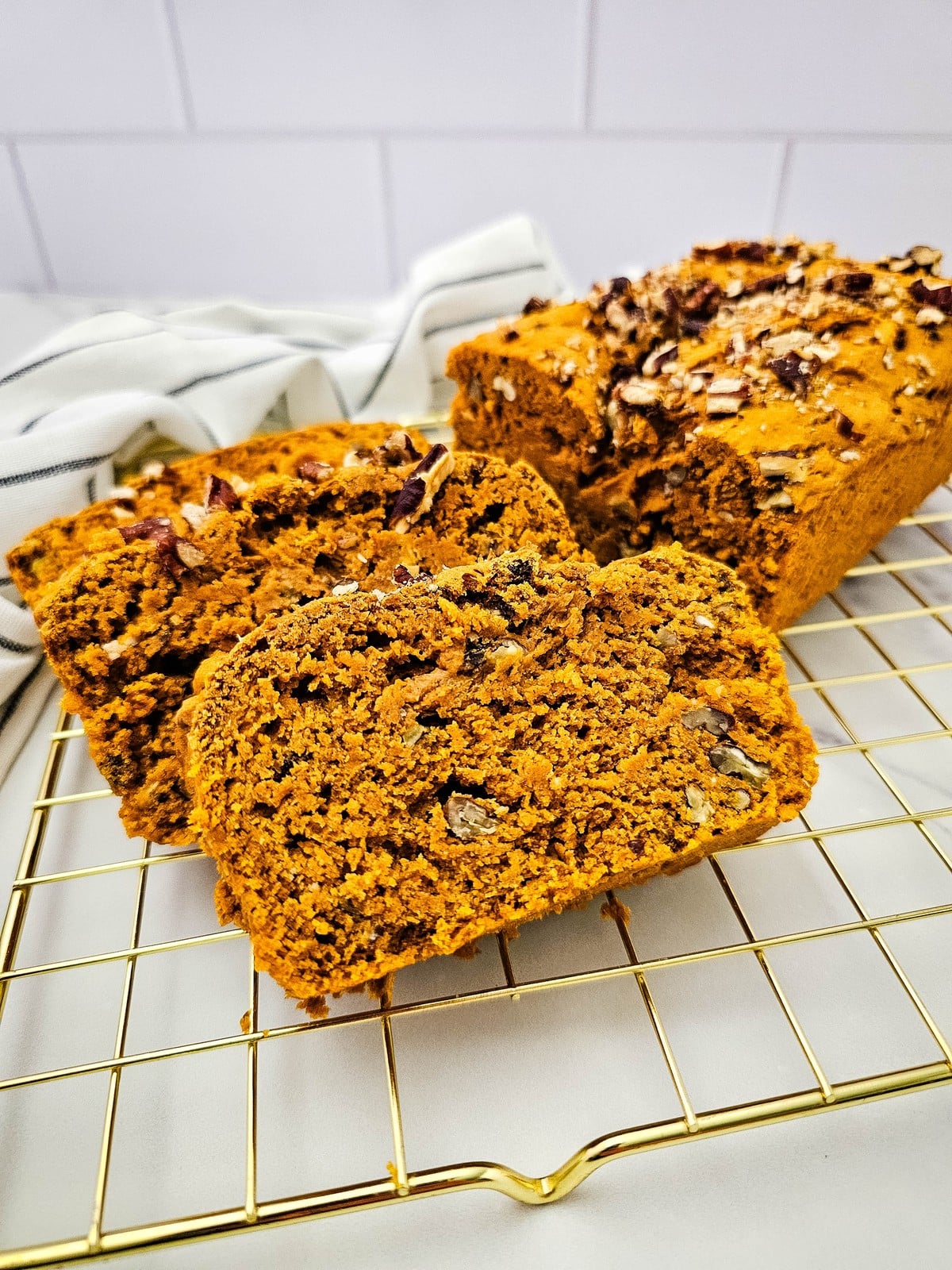 Sliced 3 ingredient pumpkin bread with a pecan top on a gold cooling rack