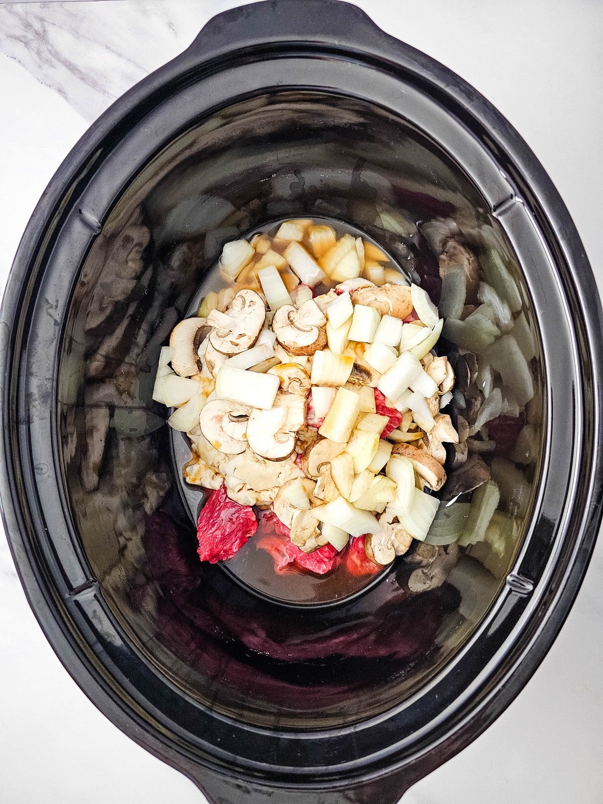 Beef broth and Worcestershire sauce poured into the slow cooker over the beef and vegetables