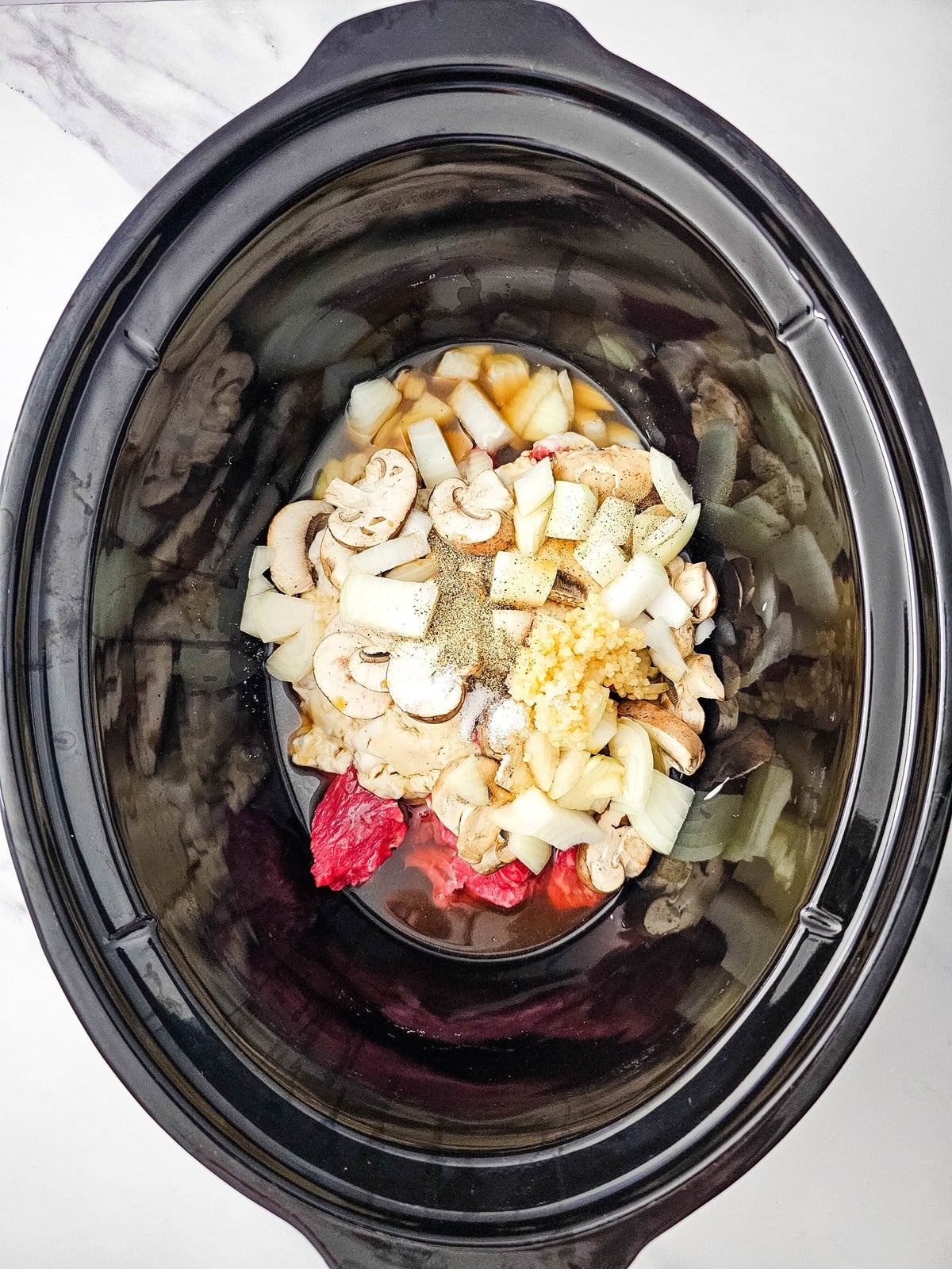 Minced garlic, salt and pepper added on top of the beef and vegetables in the slow cooker