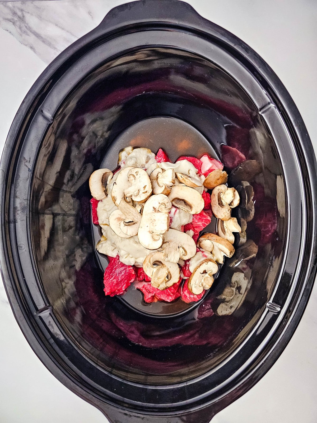 Sliced baby bella mushrooms layered over the beef and soup in the slow cooker