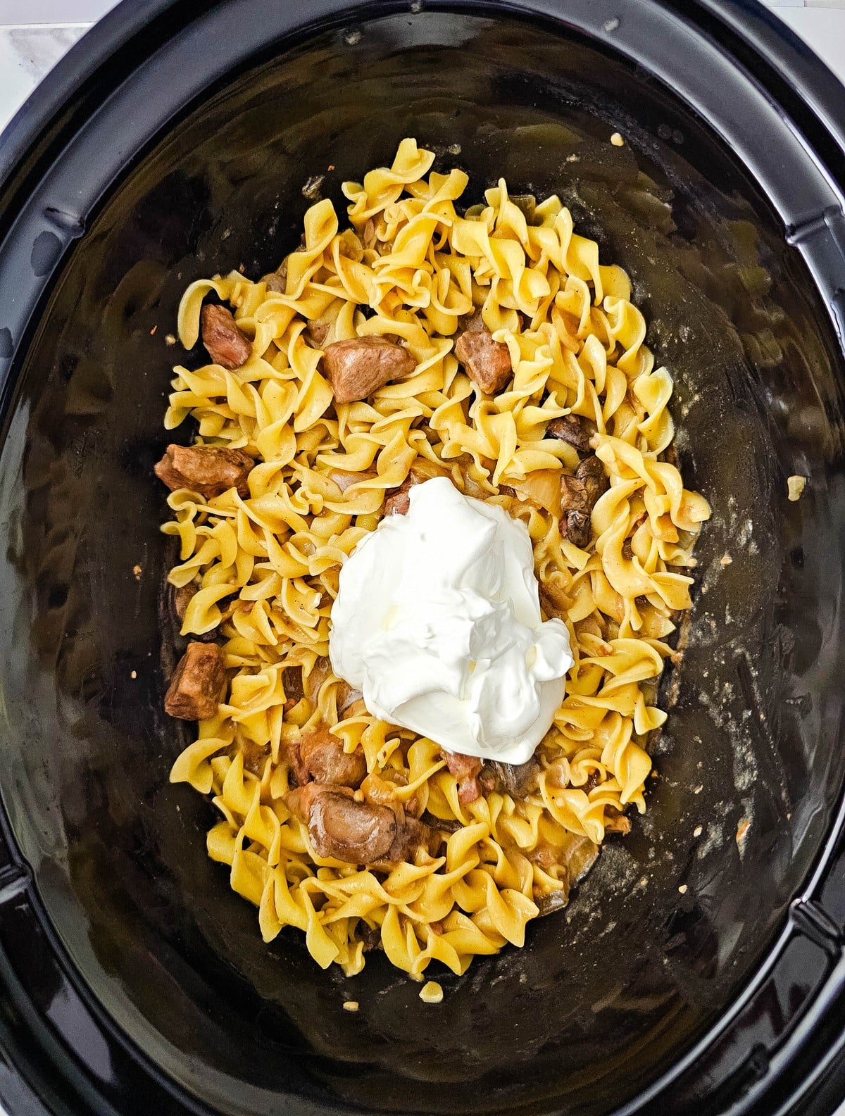 A scoop of sour cream added on top of the noodles and beef in the slow cooker
