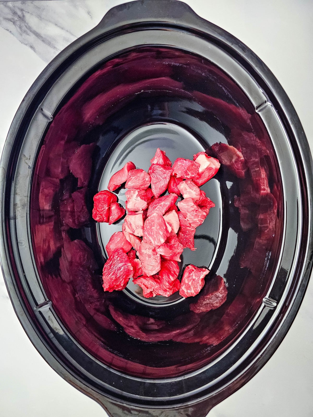 Cubed raw beef stew meat in the bottom of a black slow cooker insert