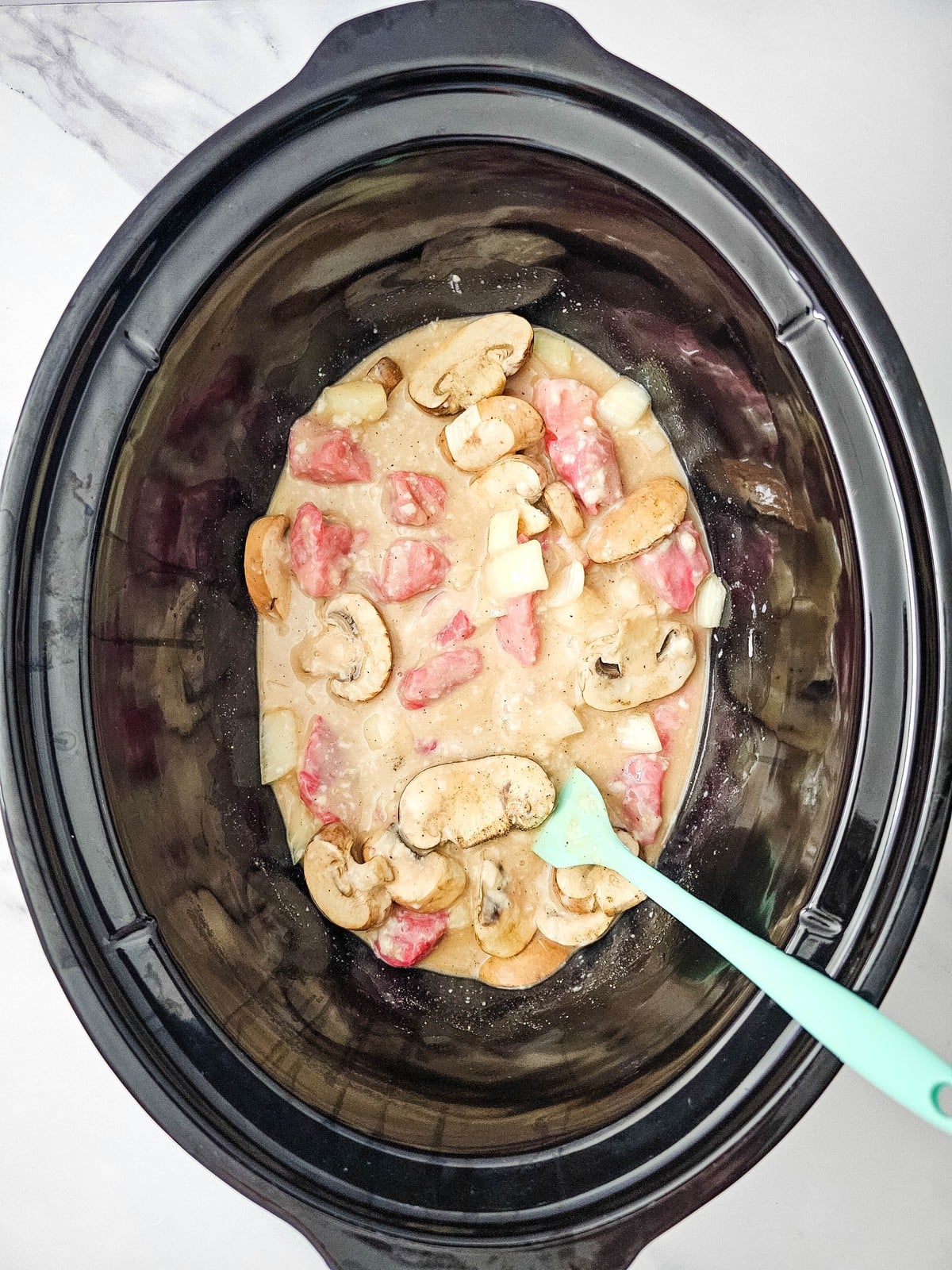 Beef stroganoff ingredients stirred together in the slow cooker with a spatula