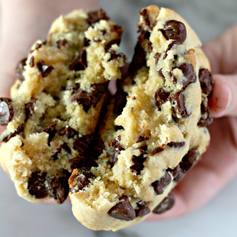 Hands pulling apart a thick chocolate chip cookie to show the soft, gooey center.