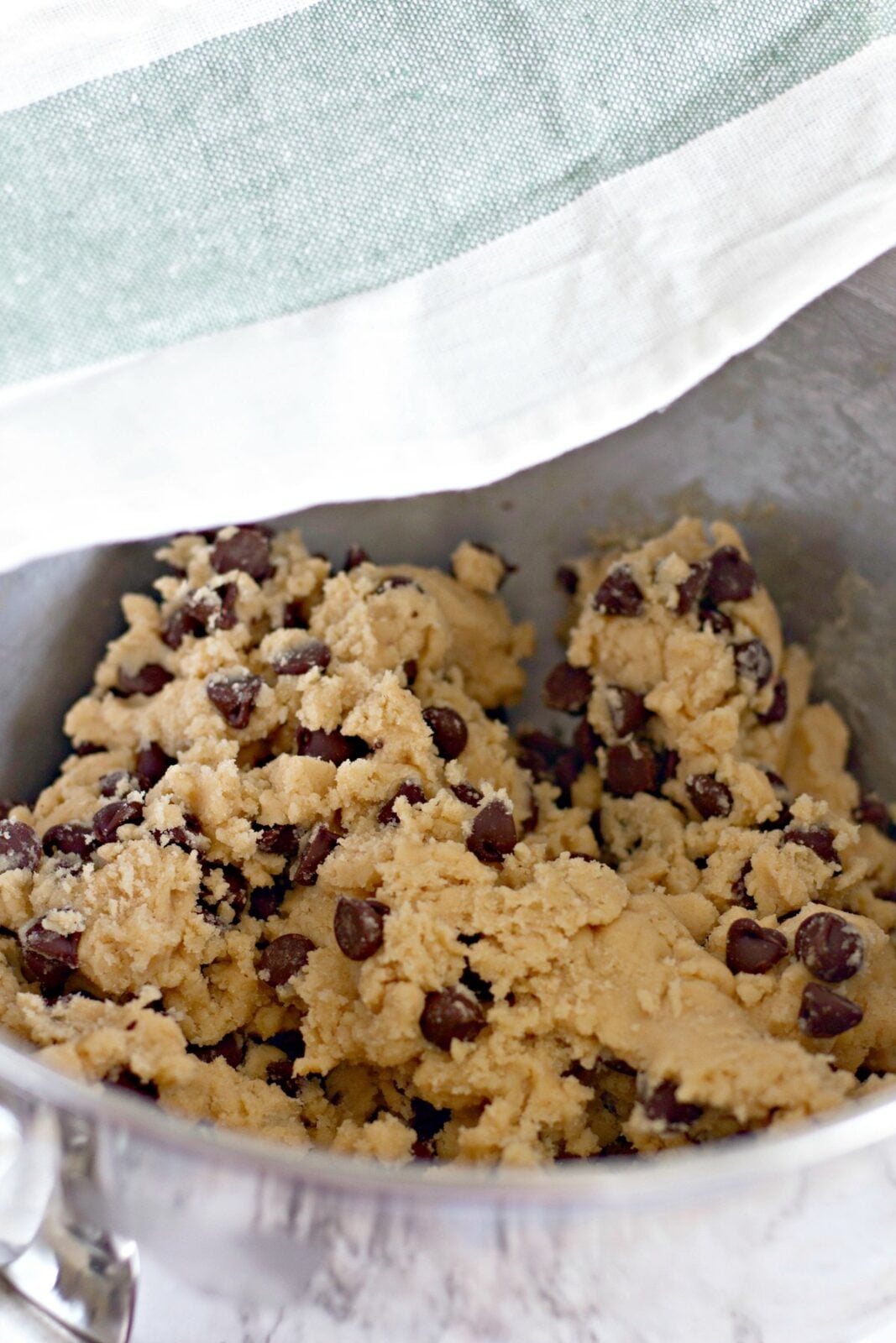 Chocolate chip cookie dough in a bowl being covered with a towel to rest.