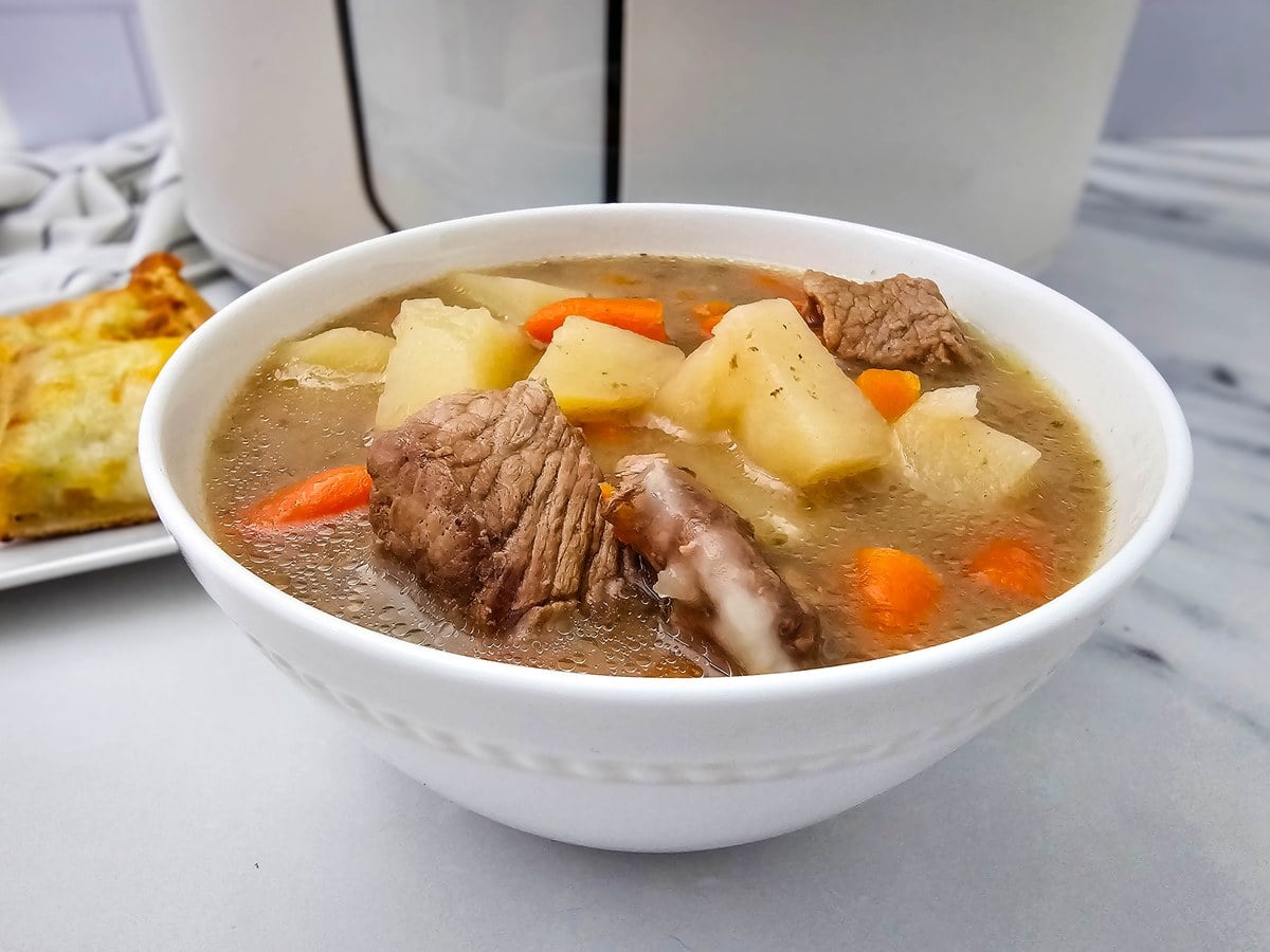 White bowl of crockpot beef stew with chunks of beef, potato and carrot