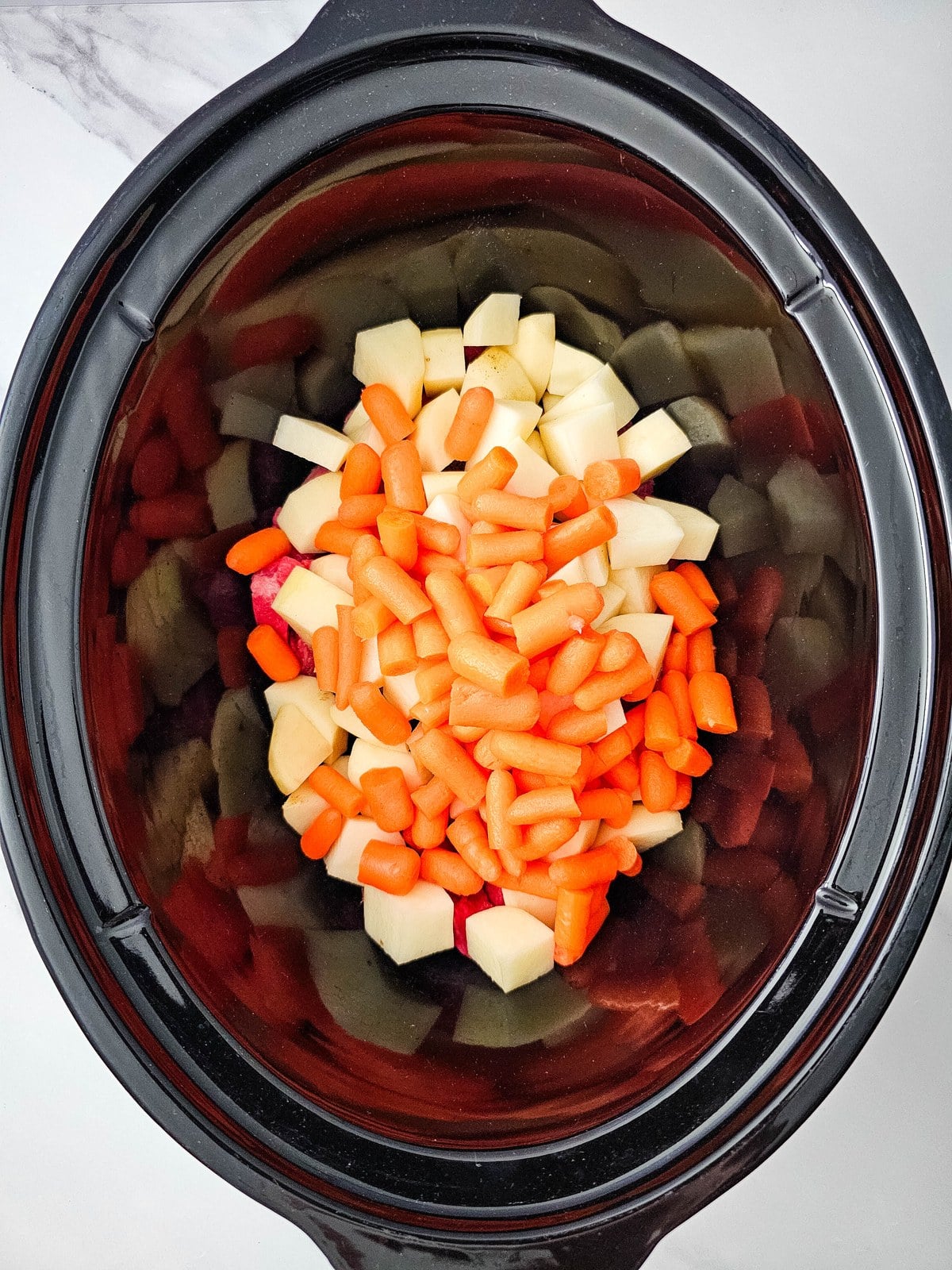 Halved baby carrots added over the potatoes and beef in the crockpot