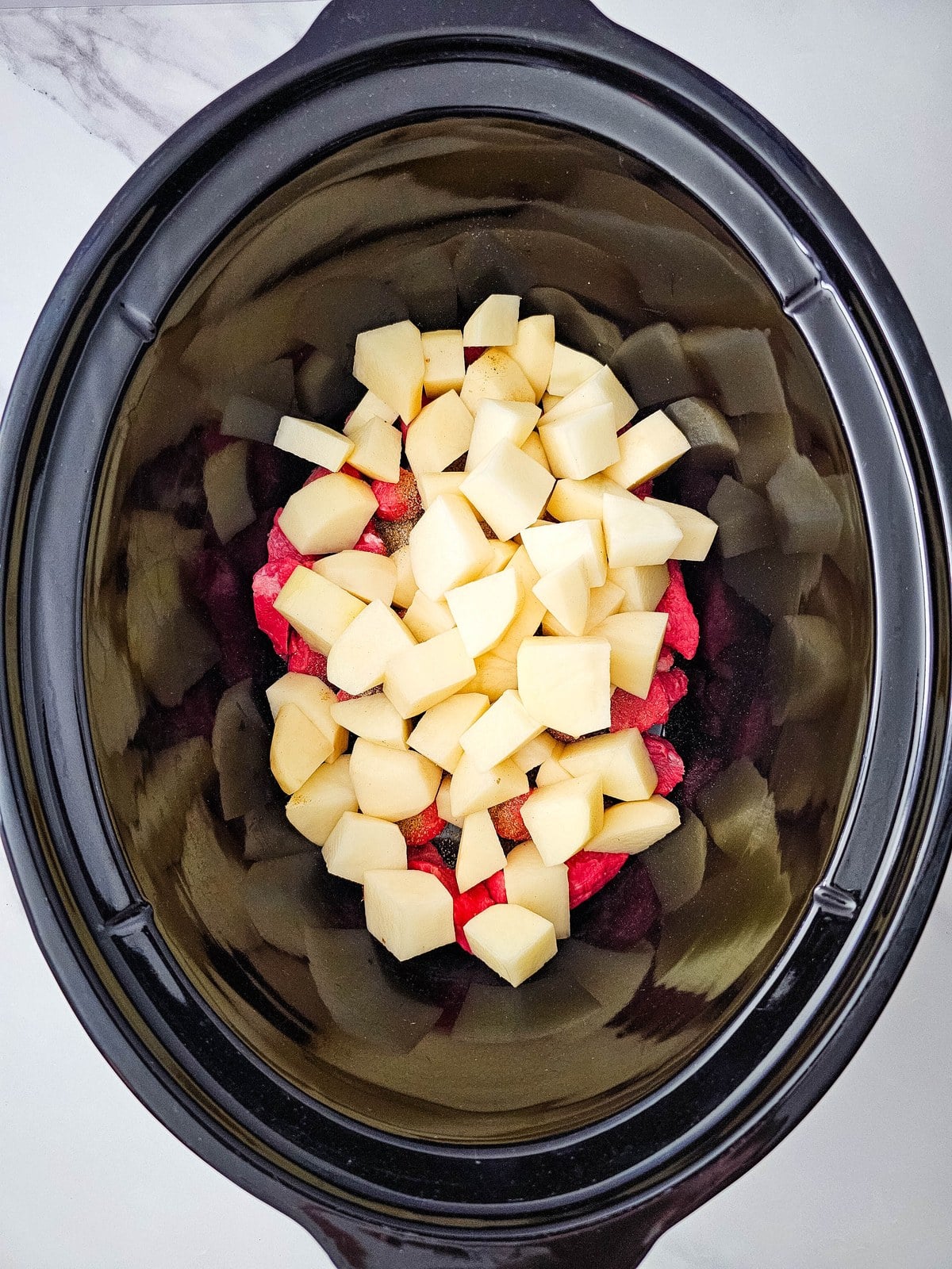 Cubed potatoes piled on top of the seasoned stew meat in the crockpot
