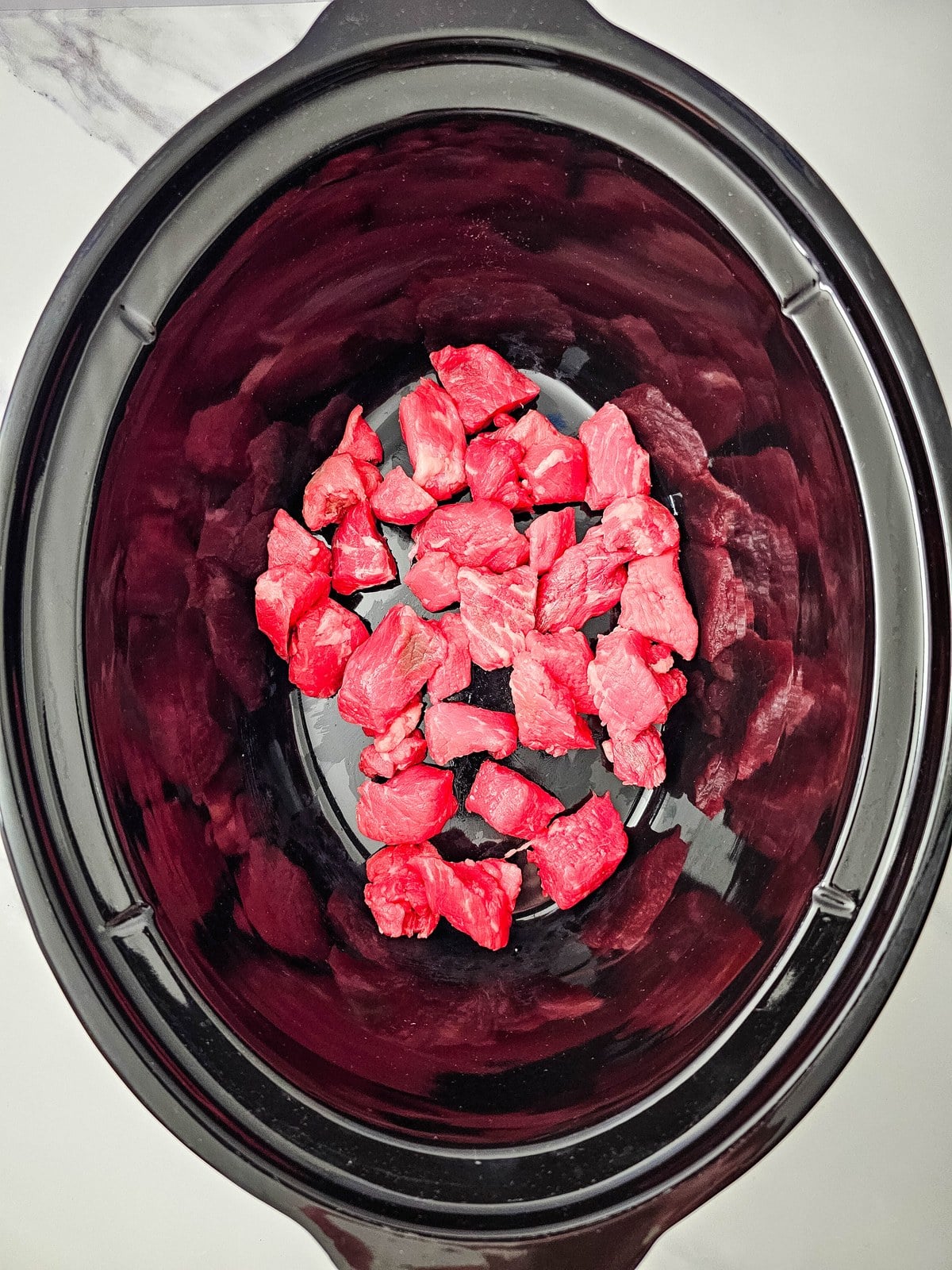 Raw stew meat in the bottom of a black crockpot