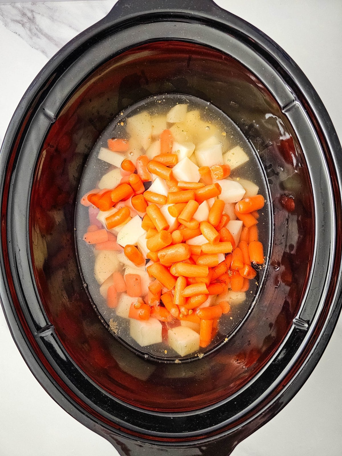 Water poured into the crockpot until the beef, potatoes and carrots are covered