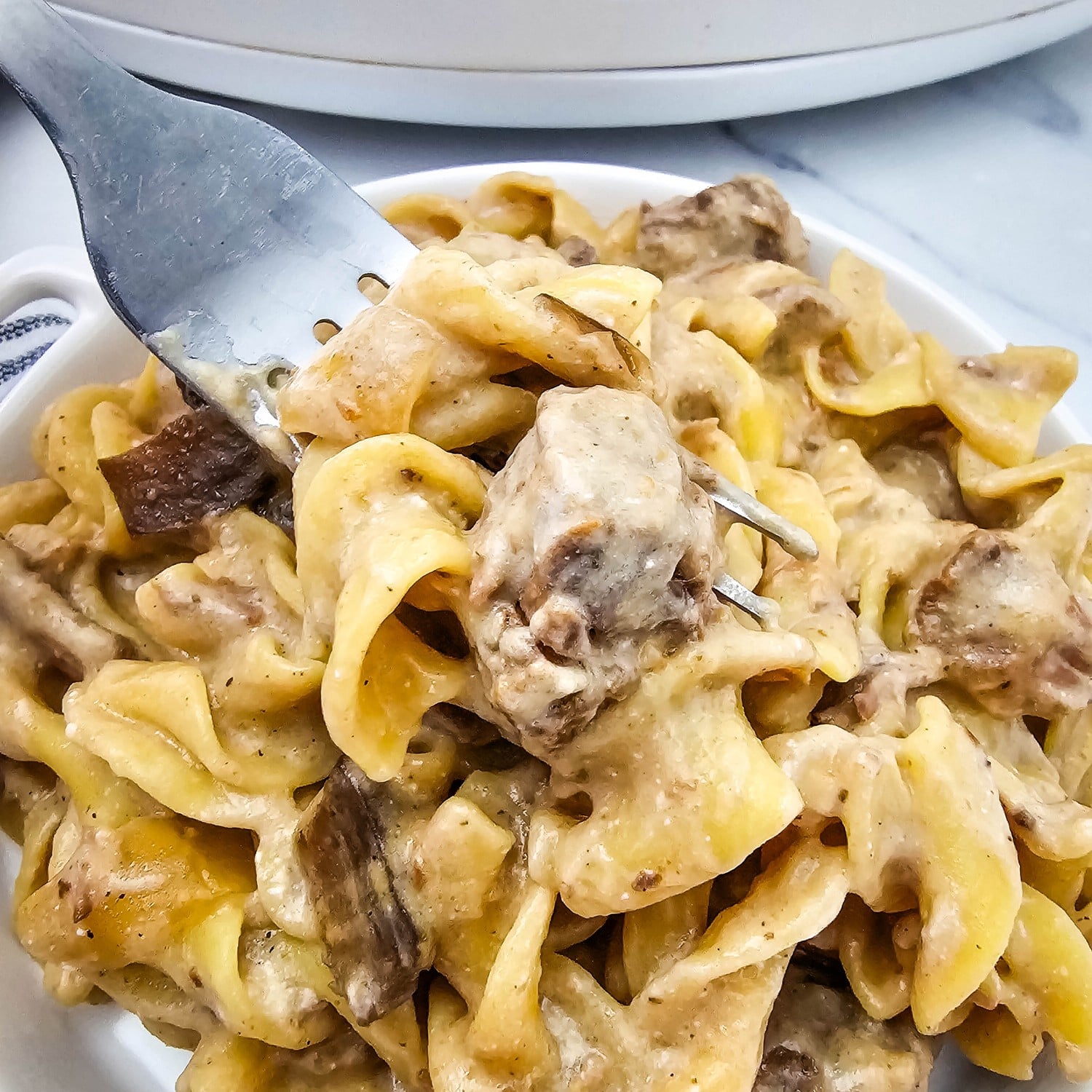 Creamy crockpot beef stroganoff over egg noodles in a white dish, close up