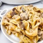 Plated crockpot beef stroganoff in a white dish with a slow cooker behind it