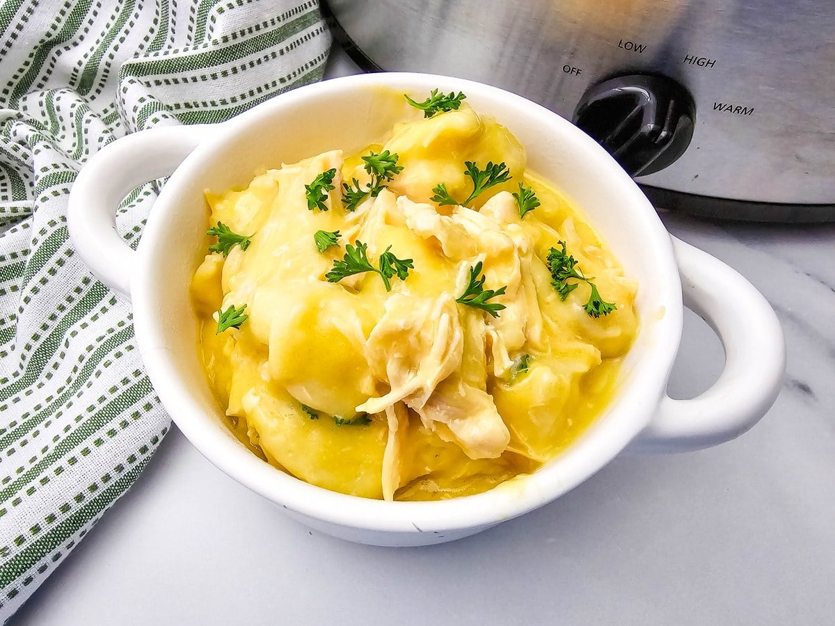 Close up bowl of crockpot chicken and dumplings with shredded chicken and chopped parsley