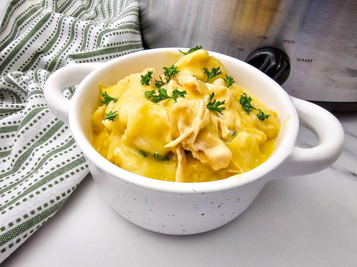 White bowl of crockpot chicken and dumplings garnished with fresh chopped parsley