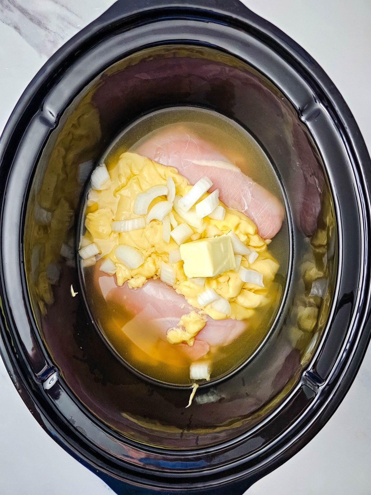 Chicken broth poured over the chicken, soup, onion and butter in the crockpot
