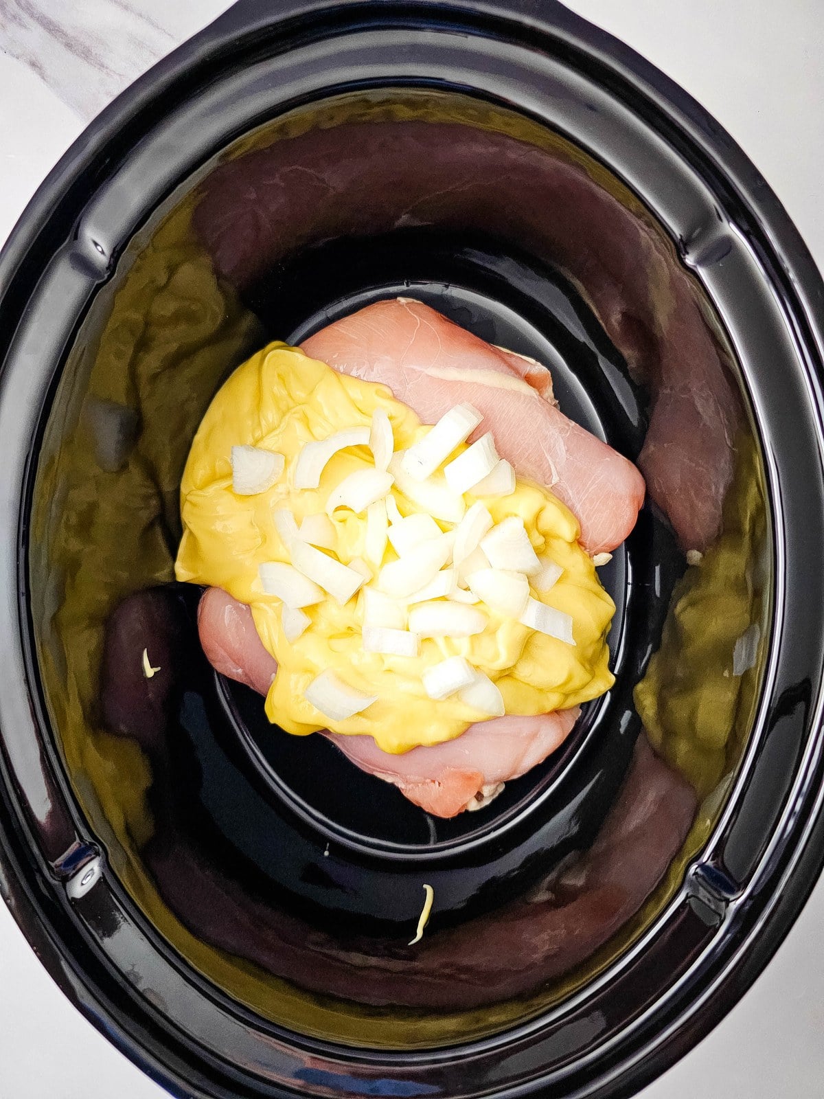 Diced onion scattered over the cream of chicken soup and chicken in the crockpot