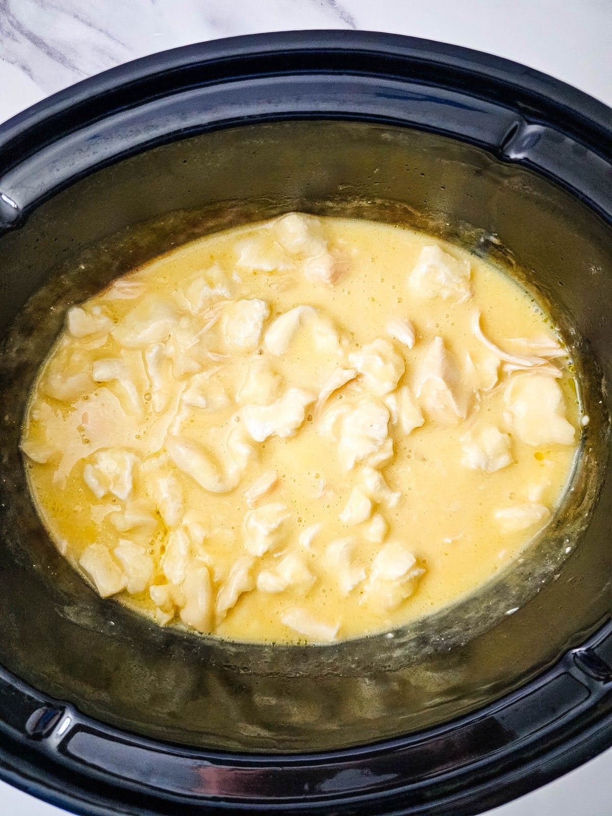 Cooked dumplings puffed up in the thickened broth in the crockpot