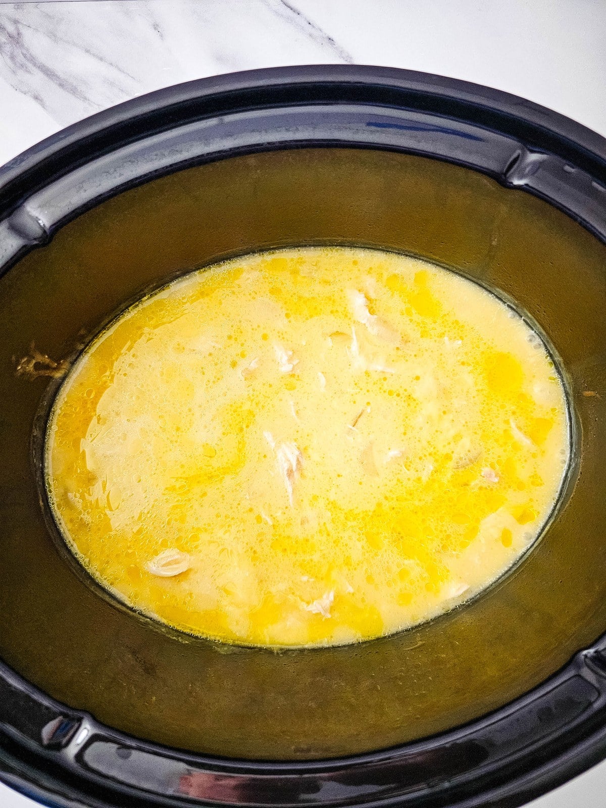 Shredded chicken in the pale broth in the crockpot after five hours of slow cooking
