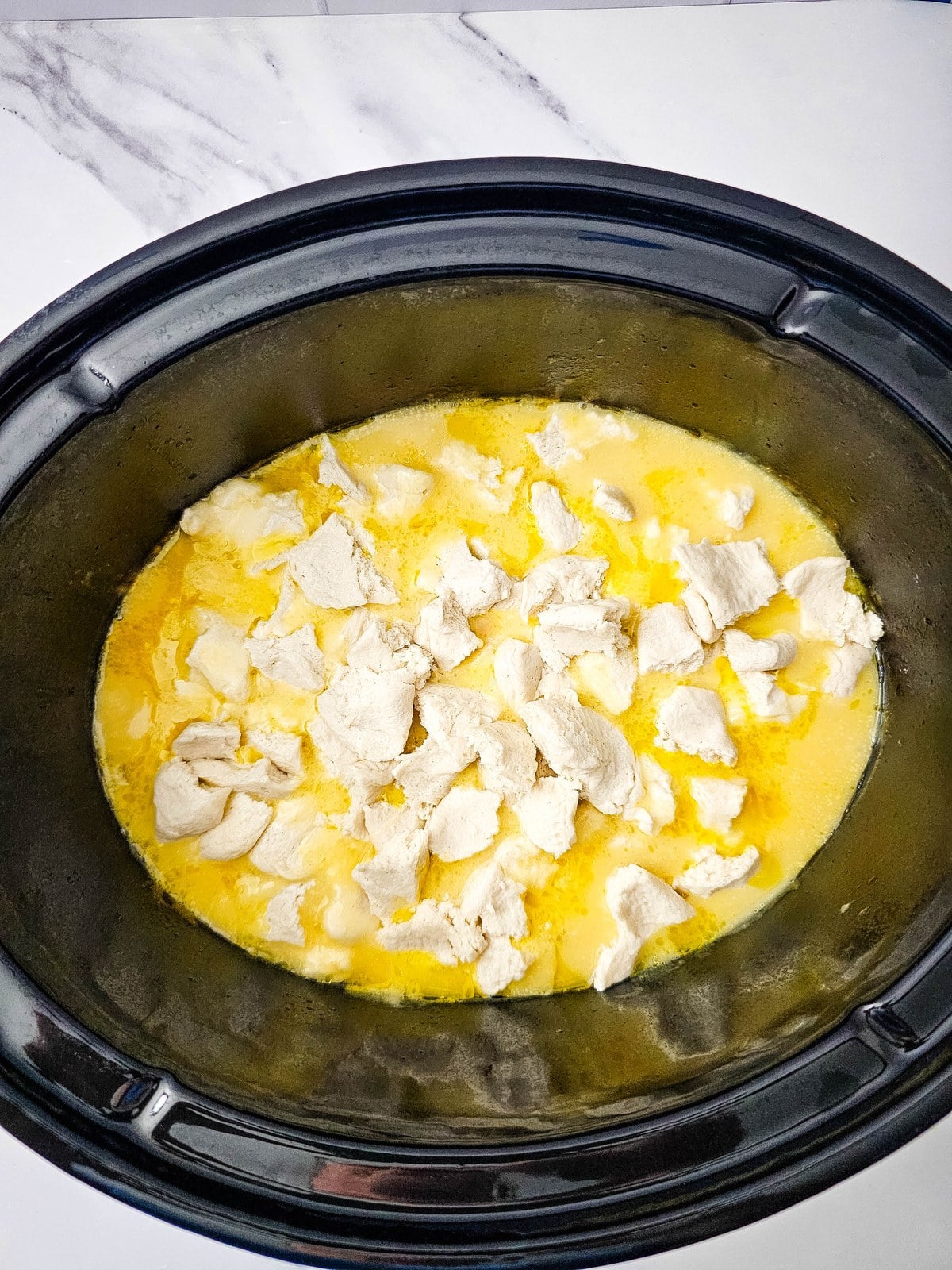 Torn pieces of refrigerated biscuit dough scattered over the broth in the crockpot