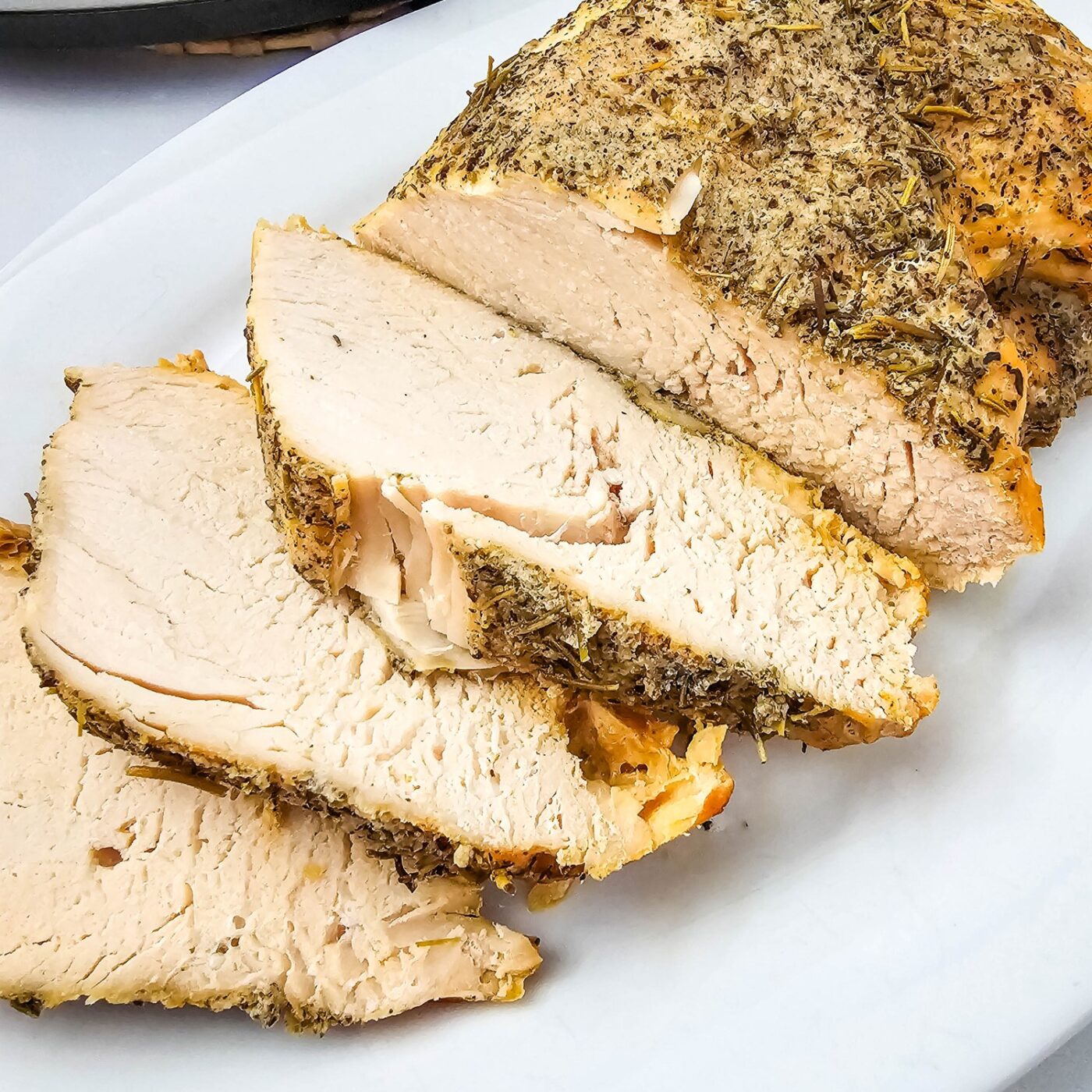 Close up of sliced crockpot turkey breast with a dried herb crust on a white platter