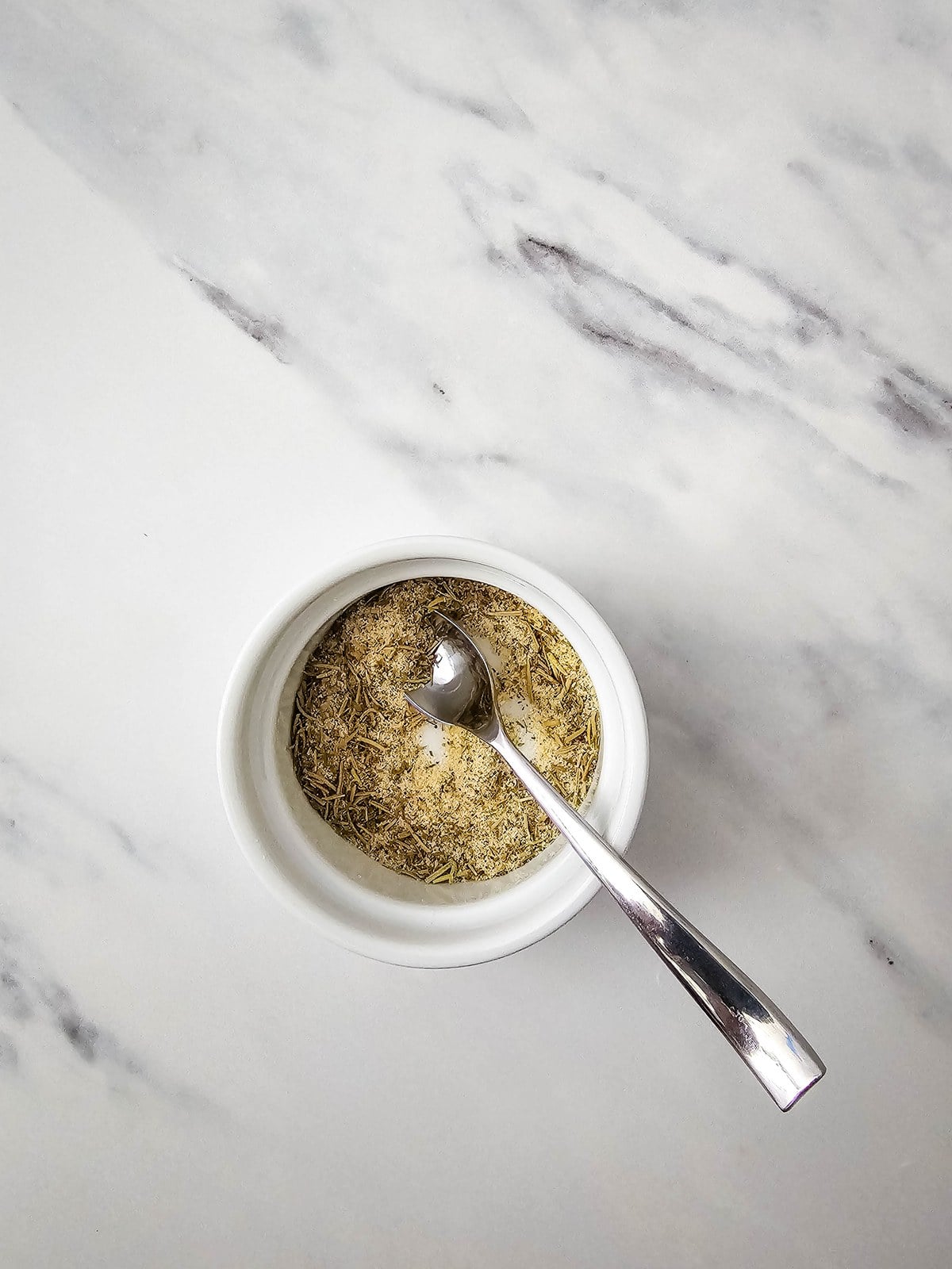 Herb seasoning mix stirred together in a small white bowl with a spoon