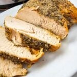 Sliced crockpot turkey breast with rosemary and thyme crust fanned on a white platter