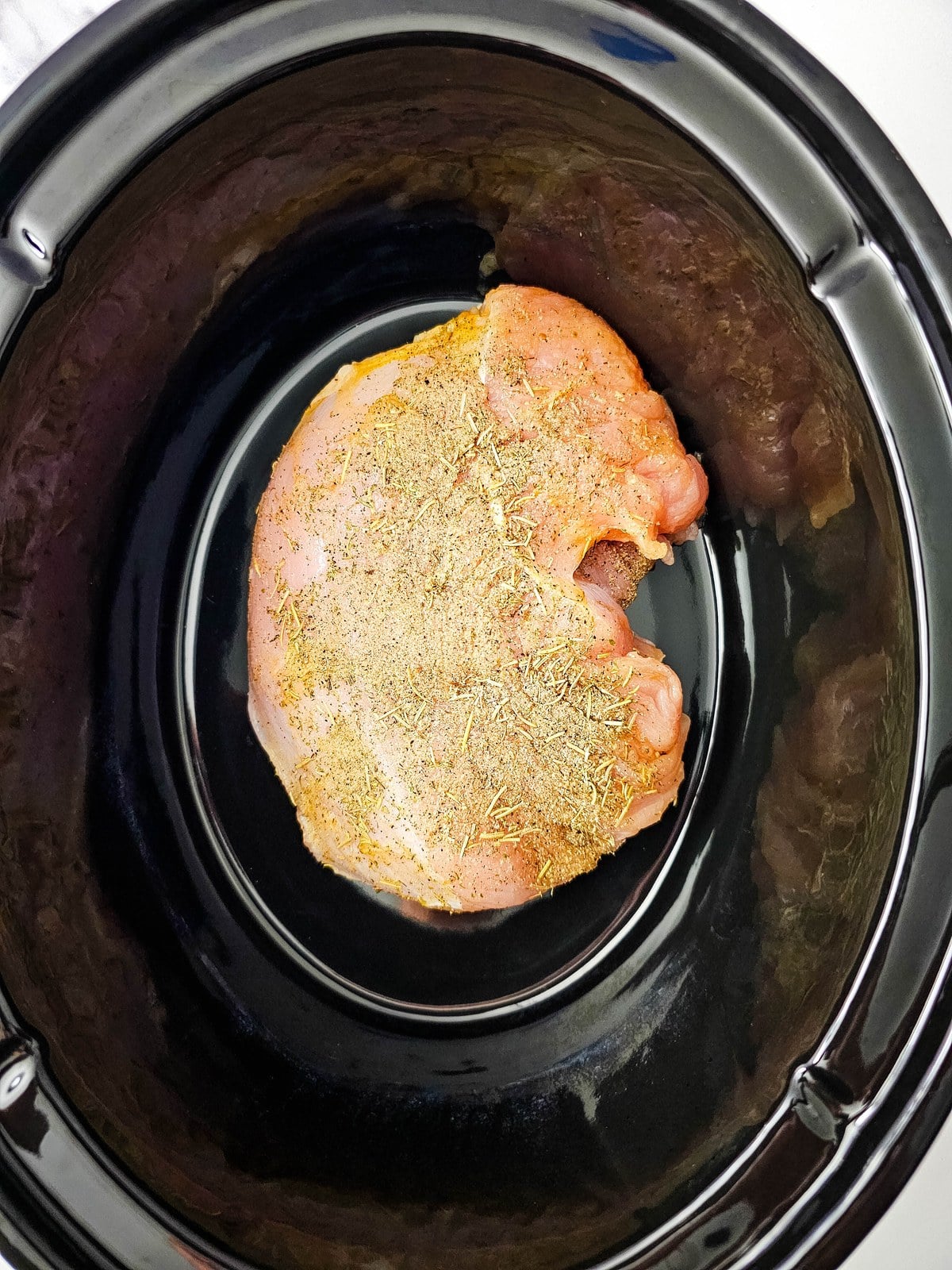 Raw turkey breast rubbed with herb seasoning in a black slow cooker insert