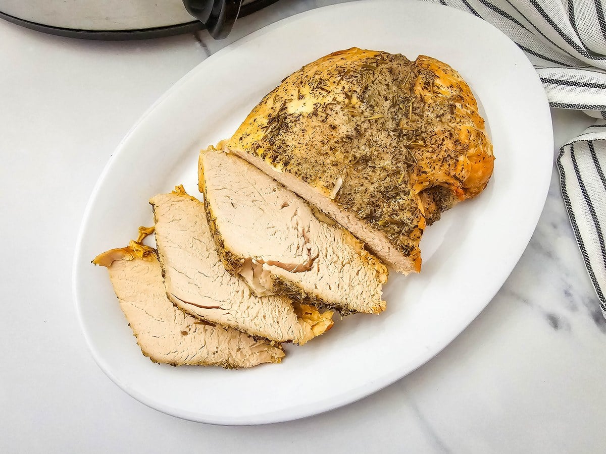 Sliced slow cooker turkey breast on a white serving platter with a striped towel