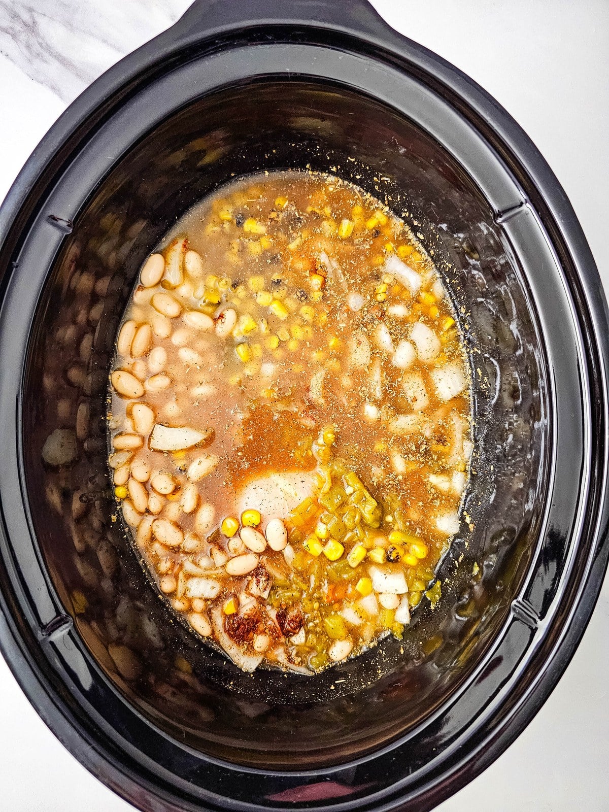 Crockpot white chicken chili ingredients covered in broth before slow cooking
