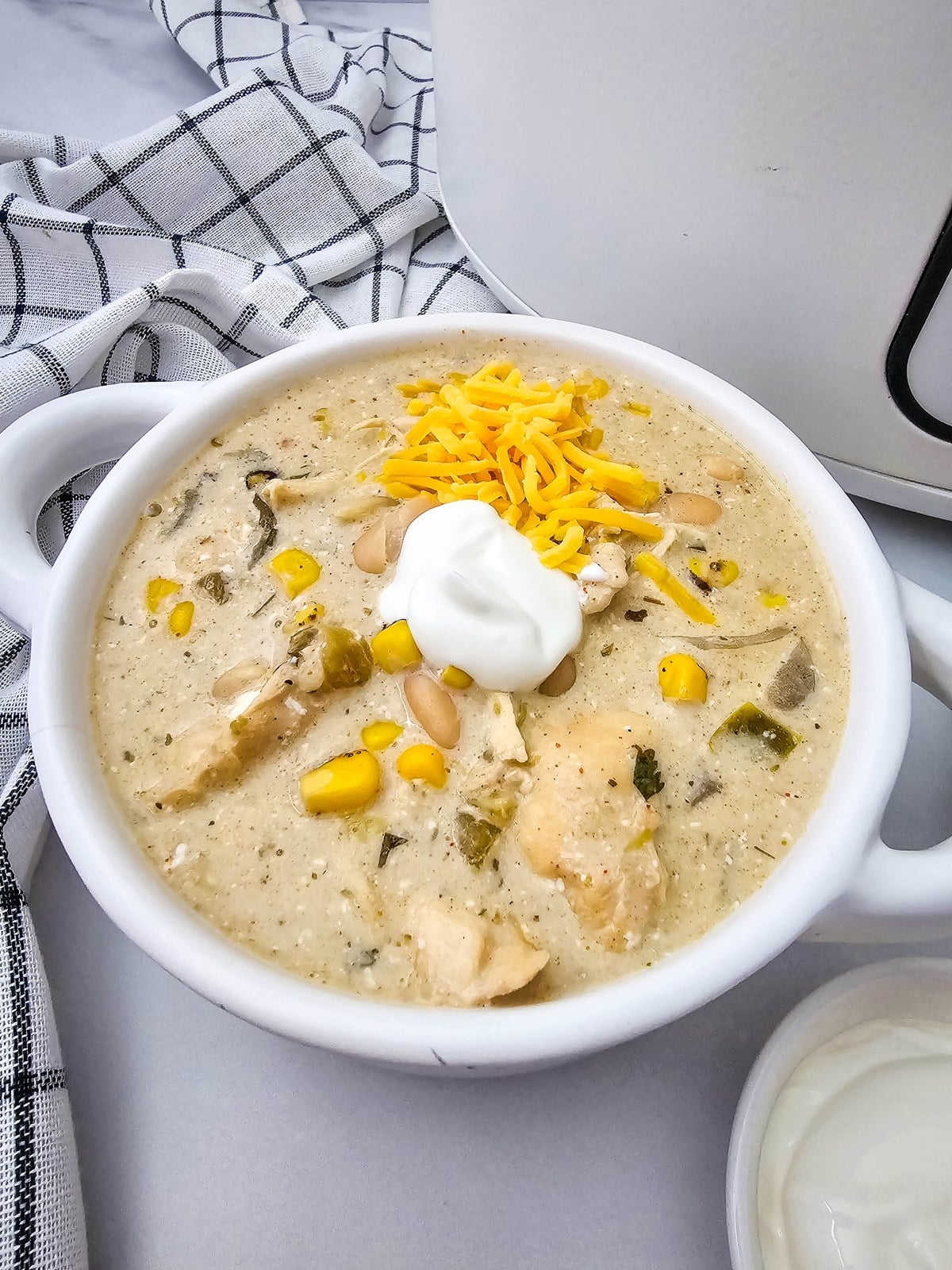 Bowl of crockpot white chicken chili topped with shredded cheddar and a spoonful of sour cream