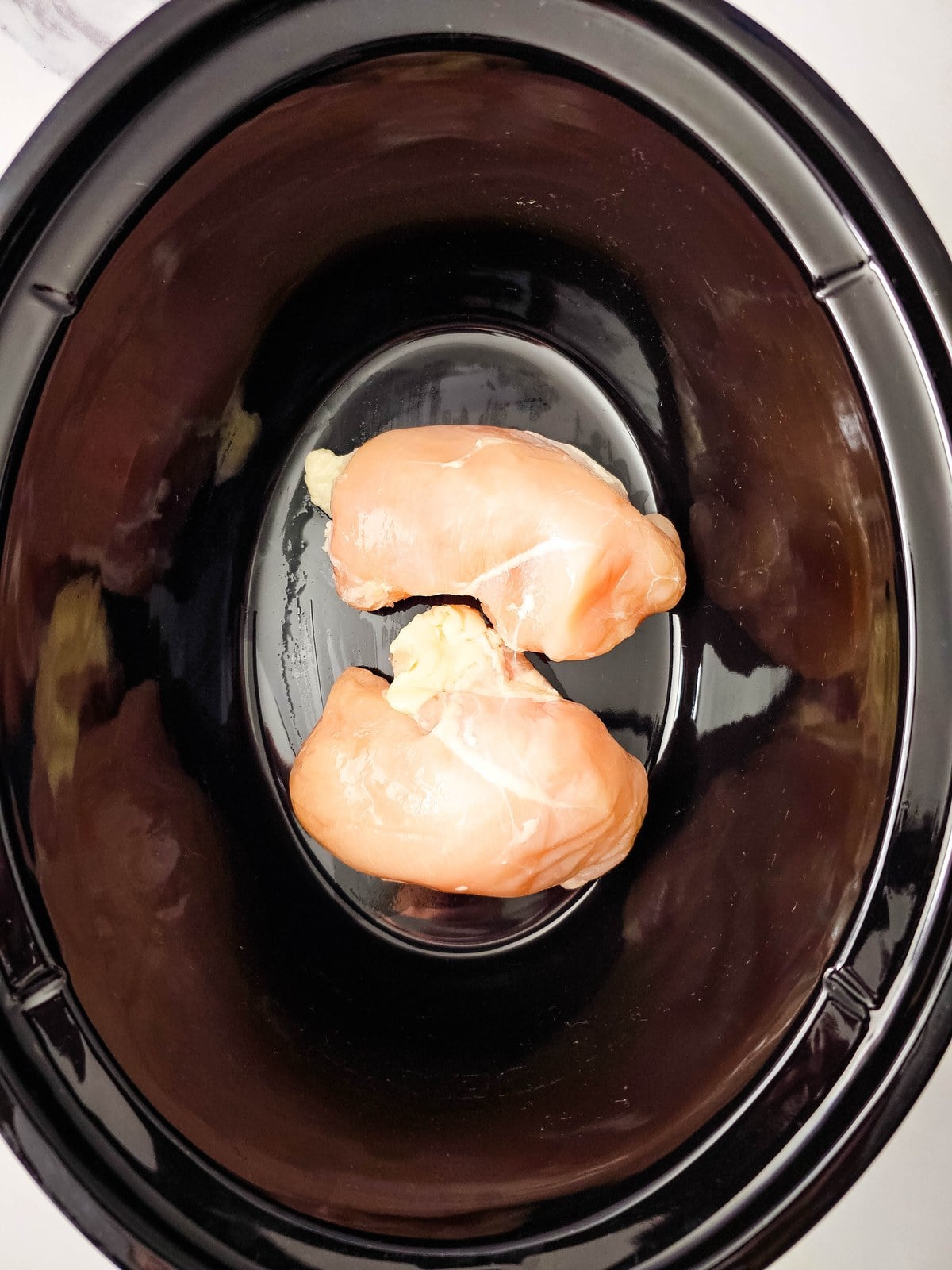 Two raw chicken breasts sitting in the bottom of a black crockpot