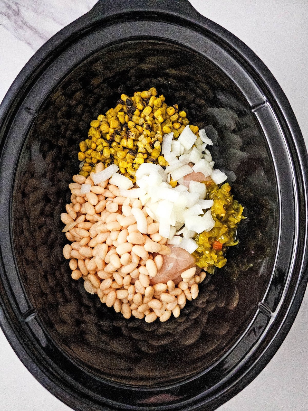 Diced onion scattered over the beans, corn and green chilis in the crockpot