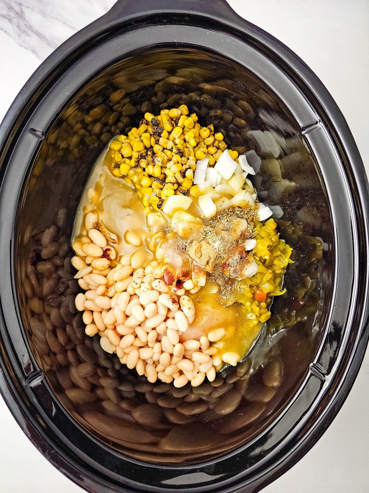 Green chili enchilada sauce poured over the ingredients in the crockpot