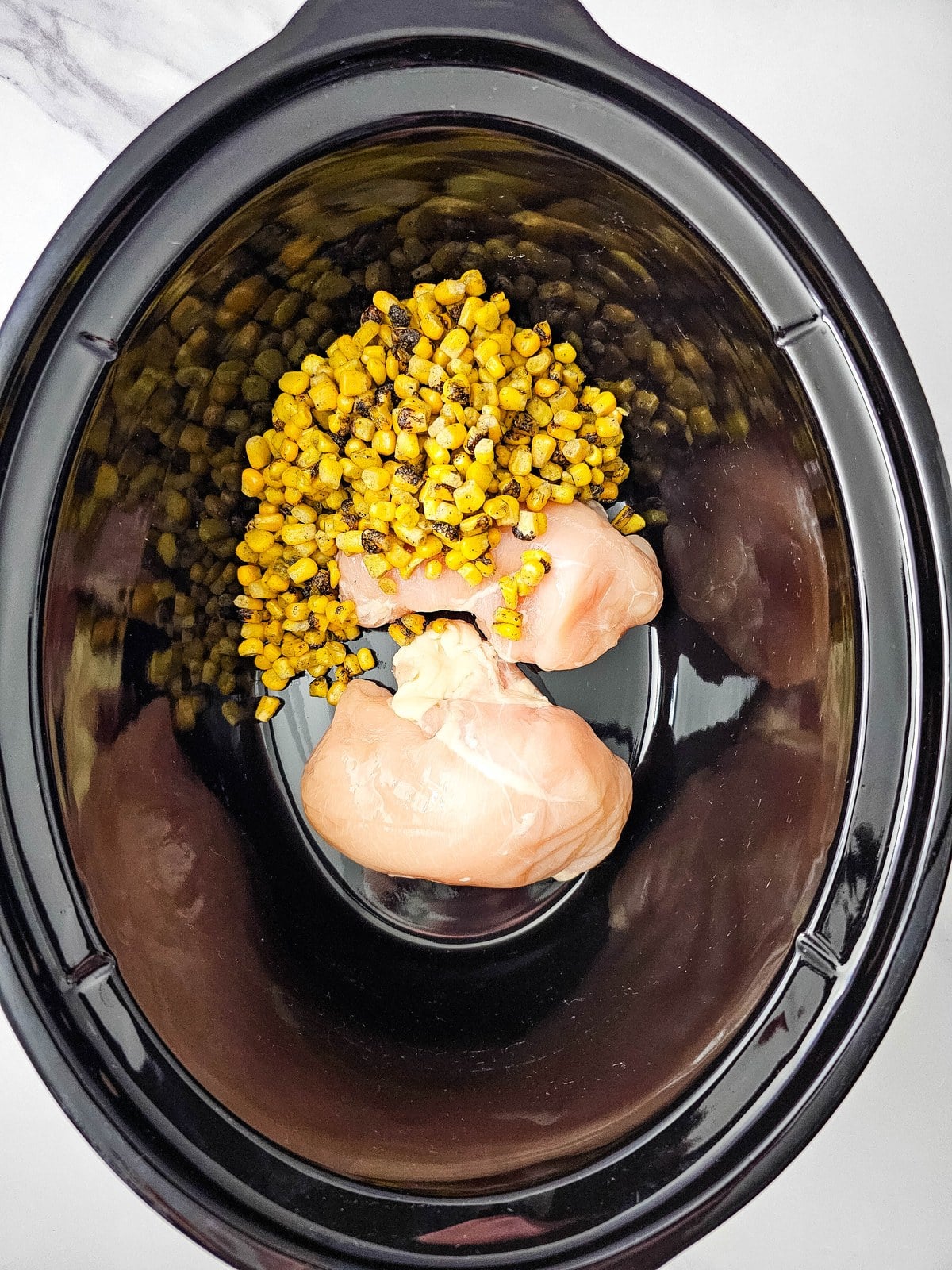 Fire roasted corn poured over the chicken breasts in the crockpot