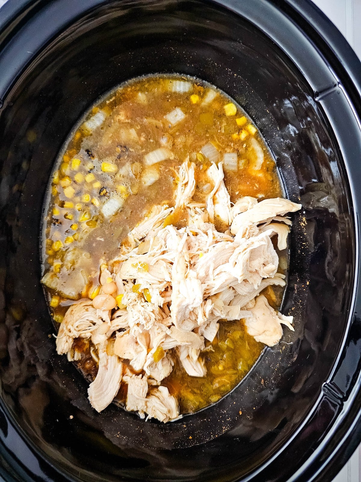 Shredded chicken added back into the crockpot of white chicken chili