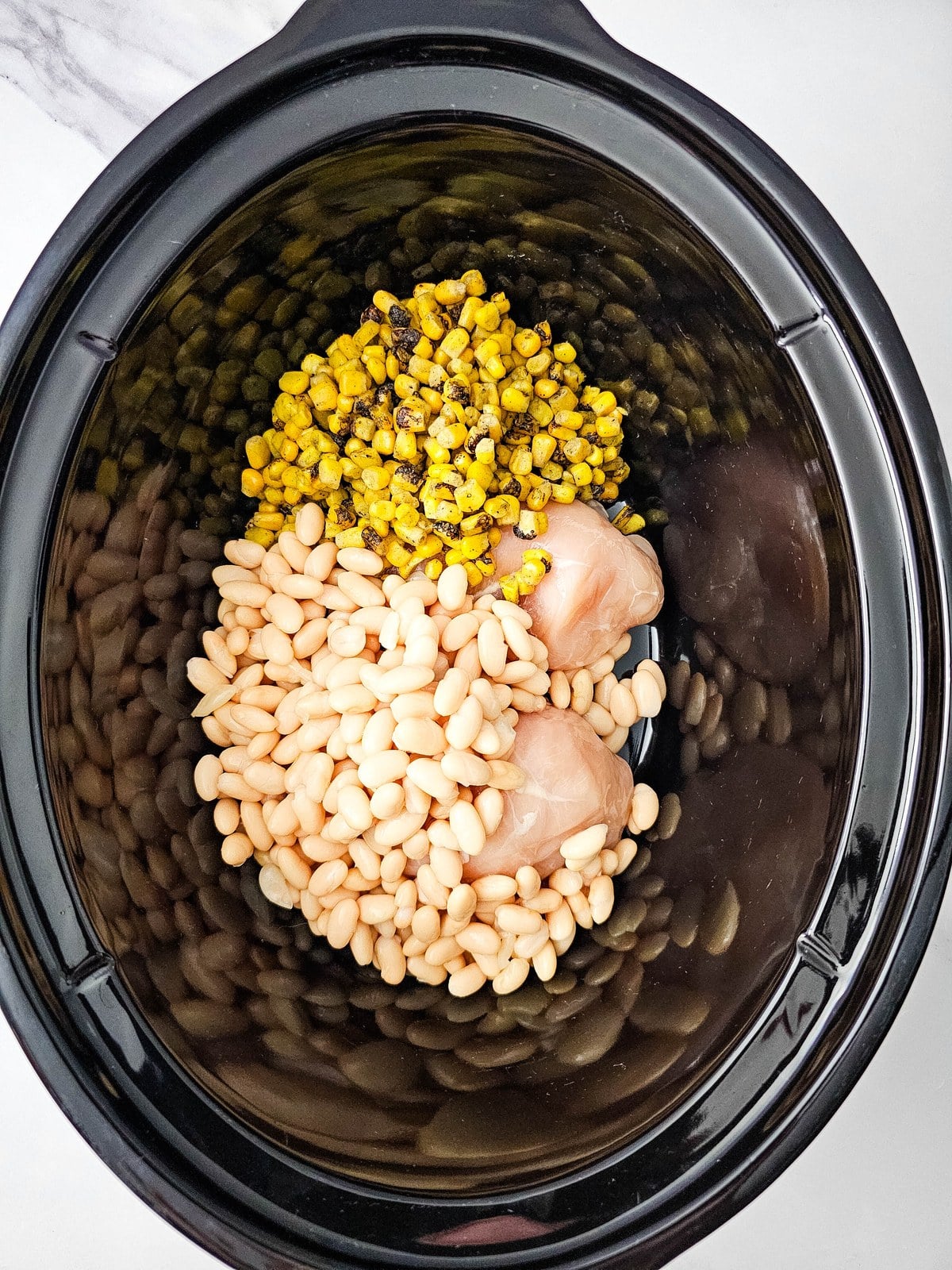 Drained white beans added on top of the corn and chicken in the crockpot