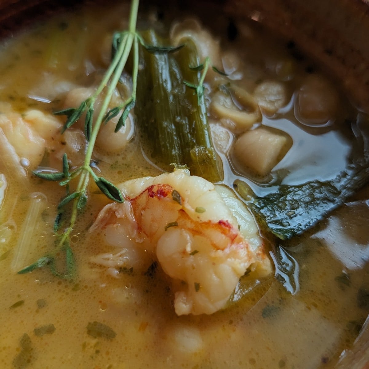 Close up of lemony shrimp stew with white beans, leeks and a sprig of thyme in a brown bowl